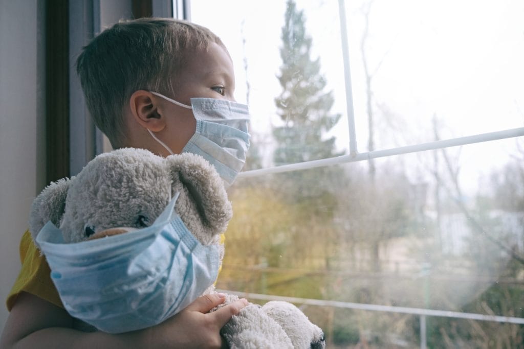 Child with teddy bear both wearing masks, looking out window, related to mold air testing service